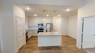 Located at 4901 SH-114 E in Northlake, Texas, this single-story home offers a clean, contemporary design with thoughtful finishes throughout. The open-concept kitchen serves as the heart of the home, showcasing white shaker-style cabinetry, granite countertops, a large central island with pendant lighting, and a full suite of stainless steel appliances including a refrigerator, gas range, microwave, and dishwasher. Wood-look plank flooring extends through the main living and kitchen areas, adding warmth and continuity to the space. The living area is bright and welcoming, featuring multiple windows that allow generous natural light and direct access to the outdoors through a glass-paneled door. Bedrooms are carpeted for comfort, each with windows that fill the rooms with natural light and ceiling fans for added convenience. The primary bathroom is well-appointed with a dual-sink granite vanity, framed mirrors, wood-look flooring, and a glass-enclosed shower. A secondary bathroom features a granite vanity and a soaking tub with marble-style tile surround. Throughout the home, neutral tones and recessed lighting create a bright, modern ambiance suited for comfortable everyday living.