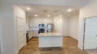 Located at 4901 SH-114 E in Northlake, Texas, this single-story home offers a clean, contemporary design with thoughtful finishes throughout. The open-concept kitchen serves as the heart of the home, showcasing white shaker-style cabinetry, granite countertops, a large central island with pendant lighting, and a full suite of stainless steel appliances including a refrigerator, gas range, microwave, and dishwasher. Wood-look plank flooring extends through the main living and kitchen areas, adding warmth and continuity to the space. The living area is bright and welcoming, featuring multiple windows that allow generous natural light and direct access to the outdoors through a glass-paneled door. Bedrooms are carpeted for comfort, each with windows that fill the rooms with natural light and ceiling fans for added convenience. The primary bathroom is well-appointed with a dual-sink granite vanity, framed mirrors, wood-look flooring, and a glass-enclosed shower. A secondary bathroom features a granite vanity and a soaking tub with marble-style tile surround. Throughout the home, neutral tones and recessed lighting create a bright, modern ambiance suited for comfortable everyday living.