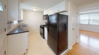 This three-floor home offers a clean, functional layout with warm hardwood flooring running consistently throughout the main and upper levels, contributing to a bright and cohesive feel across the living spaces. The main level features an open entry area with a staircase, white walls, and natural light filtering through blinds. The galley-style kitchen is well-equipped with white shaker cabinetry, dark granite-style countertops, a white subway tile backsplash, and black appliances including a gas range, refrigerator, and built-in microwave. The kitchen flows naturally into a dedicated dining area with hardwood floors and a window overlooking the outdoors. The upper level houses multiple bedrooms, each with hardwood floors, white walls, and windows that bring in natural light and views of the surrounding neighborhood. The bathroom is a standout space, featuring classic retro styling with mint green wall tiles accented by black trim, a mosaic tile floor, a wood-tone vanity, and a full soaking tub with a shower. The basement level is unfinished, offering practical utility space with an exposed ceiling, concrete block walls, a utility sink, and an electrical panel — ideal for storage or mechanical use.