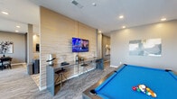 Located in Parker, Colorado, this contemporary community amenity space offers a thoughtfully designed, single-floor layout that seamlessly blends entertainment, dining, and relaxation. The space is defined by a sophisticated modern aesthetic, with neutral gray tones, textured accent walls, and warm metallic finishes throughout.

The game and lounge area anchors one end of the space, highlighted by a striking textured wood-panel feature wall with a wall-mounted flat-screen TV and a sleek bar-height console with industrial stools. A full-size pool table with a vibrant blue felt surface adds a focal point for entertainment.

The living area offers an inviting arrangement of tufted leather sofas, teal velvet accent chairs, and a statement chandelier, all bathed in natural light streaming through expansive floor-to-ceiling windows that open to outdoor views of the surrounding community.

The kitchen and dining zone features a generous island with a polished quartz countertop, leather bar stools, and elegant brass pendant lighting. Built-in shelving with a wood-panel surround and a mounted TV make this a functional yet stylish gathering hub.

A dedicated dining nook, carpeted and framed by large sliding glass doors, provides an intimate setting with direct outdoor views. Throughout, the patterned carpeting, large-format tile flooring, and curated artwork contribute to a cohesive, upscale communal atmosphere.