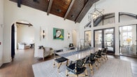 Located at 40 Brisa Ave in St. Augustine, Florida, this single-story community space delivers an impressive blend of architectural grandeur and refined interior design. The centerpiece of the space is a dramatic great room boasting soaring vaulted ceilings with rich, dark-stained exposed wood beams and a striking tongue-and-groove wood ceiling, creating an atmosphere of warmth and elegance. Rich hardwood flooring flows continuously throughout, anchoring the open, light-filled layout.

The expansive dining area accommodates a grand long table surrounded by woven leather and wood chairs, illuminated by geometric pendant chandeliers and flanked by tall black-framed French doors that invite natural light and outdoor views. Arched doorways lend a Mediterranean-inspired architectural detail, seamlessly connecting each area of the space.

A cozy lounge area features coffered wood beam ceilings, a wall-mounted display, and curated seating. A fireplace with a herringbone tile surround and a prominent white mantle serves as a focal point in an intimate sitting nook. A well-appointed kitchen bar area showcases a dramatic textured metallic tile accent wall, a white island with bar seating, pendant Edison bulbs, and beverage stations, offering direct access to an outdoor terrace.