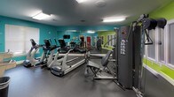 Located at 1005 W Trade St in Charlotte, NC, this fitness center is a well-equipped, single-floor space designed to support a full range of workout routines. The interior is immediately striking thanks to its bold color palette — vibrant lime green and teal accent walls create an energetic atmosphere enhanced by bright overhead fluorescent lighting and rubber flooring throughout.

The strength training area features a multi-function cable machine alongside a dedicated dumbbell rack stocked with a variety of free weights, providing ample options for resistance training. A full-wall mirror runs along one side of the space, visually expanding the room and allowing users to monitor their form during workouts.

The cardio zone is outfitted with multiple treadmills and elliptical machines, all positioned for easy access. A wall-mounted flat-screen television is conveniently placed for viewing during cardio sessions, and a window with blinds allows for natural light. Informational signage and a small wall-mounted shelf add practical utility to the space.

An adjacent restroom is finished with bold orange walls, a checkered tile floor, a pedestal sink, and grab bar accessibility features, ensuring convenience and inclusivity for all users.

Overall, this fitness center offers a compact yet comprehensive workout environment with a lively, motivating design well-suited to its urban Charlotte location.