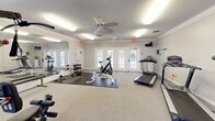 Located at 101 Montrose Ct in Dothan, Alabama, this fitness center offers a well-equipped exercise space designed to support a full range of workout routines. The room features a light neutral color palette, crown molding, and a textured ceiling, all contributing to a clean and functional atmosphere. Two ceiling fans provide steady air circulation throughout the space, complementing the flush fluorescent lighting overhead.

Natural light fills the room through a combination of large multi-pane windows and elegant French doors, the latter offering direct access to an outdoor pool area. A full-length wall mirror on one side of the room visually expands the space and serves as a practical aid during strength training exercises.

The fitness center is equipped with a diverse array of exercise equipment, including multiple treadmills, a stationary upright bike, a stair climber, and an elliptical machine for cardiovascular workouts. A multi-function cable resistance machine supports a wide variety of strength exercises, while a dumbbell rack stocked with a full set of free weights and an adjustable weight bench with a barbell provide dedicated strength training options. Protective rubber floor mats are positioned in the free weight area for safety and floor preservation.

A wall-mounted flat-screen television, a water cooler, and a posted workout information board round out the amenities, making this a comprehensive and convenient fitness facility.