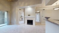 Located at 9898 Colonnade Boulevard in San Antonio, Texas, this 2-bedroom, 2-bathroom residence offers a thoughtfully designed single-floor layout with a warm, neutral color palette throughout. The open living area serves as the heart of the home, anchored by a classic white-mantled fireplace with tile surround and plush wall-to-wall carpeting. The kitchen features granite countertops, white cabinetry, track lighting, and a breakfast bar peninsula that connects seamlessly to the living space, with hardwood-style flooring adding a polished touch. The primary bedroom impresses with vaulted ceilings, a ceiling fan, and sliding glass doors opening to a private balcony with tree-lined views. A walk-in closet with built-in shelving and hanging rods provides ample storage. The second bedroom is highlighted by a striking arched window that floods the room with natural light and includes a built-in desk and shelving unit, ideal for a home office setup. Both bathrooms are finished with granite-topped white vanities and hardwood-style flooring, with one bathroom offering a full soaking tub. A connecting hallway ties all spaces together efficiently, completing this comfortable and well-appointed San Antonio residence.