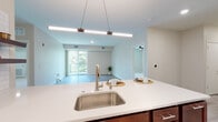 This well-appointed single-floor residence offers a thoughtfully designed open-concept layout that seamlessly connects the kitchen, dining, and living areas. The kitchen is a standout feature, showcasing rich dark wood cabinetry, stainless steel appliances including a French door refrigerator and microwave, a classic white subway tile backsplash, and an expansive white quartz island with bar seating and pendant lighting overhead — ideal for both meal prep and casual dining. Light wood-style vinyl plank flooring flows throughout the main living areas, complementing the neutral, warm-toned walls.

The living area is generously proportioned and filled with natural light, with direct access to a private balcony offering lush green views. The bedroom features plush carpeting, a ceiling fan, and a window overlooking the surrounding greenery, creating a calm and restful retreat. The bathroom is elegantly finished with decorative patterned tile flooring, a dual-sink vanity with dark countertops, backlit mirrors, and a sleek frameless glass walk-in shower with white tile surround. A dedicated in-unit laundry room with full-size washer and dryer adds a practical and convenient touch to this modern, move-in-ready space.