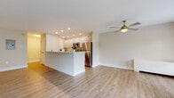 This well-appointed single-floor residence offers a clean, modern aesthetic defined by light hardwood flooring, crisp white walls, and an open-concept layout that promotes a seamless flow throughout the living spaces. The kitchen is a functional highlight, featuring white cabinetry, a full suite of stainless steel appliances including a refrigerator, microwave, and range, complemented by a generous peninsula with a white countertop that serves as both a prep area and a casual dining space. Recessed lighting overhead keeps the kitchen bright and welcoming. A dedicated butler's pantry or utility corridor provides additional counter and cabinet storage, finished with wood-toned lower cabinetry and subway tile backsplash detailing. The spacious living area benefits from a ceiling fan and large sliding glass doors that open onto a private balcony, flooding the room with natural light and offering tranquil views of surrounding greenery. An additional room features dual windows that further enhance the natural light. The bathrooms are finished with large-format neutral tiles, with one bathroom offering a full soaking tub and shower combination. The overall ambiance is contemporary, clean, and airy, making excellent use of natural light and a cohesive neutral palette throughout.