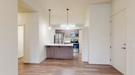 This single-floor residence offers a practical and modern layout with 2 bedrooms and 2 bathrooms. The open-concept kitchen and living area serves as the heart of the home, featuring light wood-style flooring, a kitchen island with a white countertop and built-in sink, pendant lighting, and stainless steel appliances including a refrigerator, range, and microwave. A louvered closet panel provides additional storage within the kitchen area.

The living room benefits from natural light through a window and exterior door, enhanced by a wall-mounted mini-split climate control unit and durable wood-style flooring. Both bedrooms are carpeted and offer a clean, neutral palette with windows that invite natural light. The primary bedroom includes its own wall-mounted mini-split unit and dedicated closet access. A walk-in closet with wire shelving and carpet flooring provides ample storage.

Both bathrooms are finished with wood-style flooring, vanities featuring white countertops and warm cabinetry, and full tub/shower combinations with brushed nickel fixtures. A hallway connects the rooms, contributing to an efficient and cohesive flow throughout the residence.