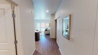 This well-appointed apartment at 12623 Bridgeport Way SW in Lakewood, Washington, offers a thoughtfully designed single-floor layout that balances comfort and modern style. A welcoming entry hallway with wood-look flooring and recessed lighting leads into the heart of the home, where a framed mirror and clean white walls set a bright, contemporary tone.

The kitchen is a standout feature, showcasing dark espresso cabinetry contrasted against crisp white countertops and a full suite of stainless steel appliances, including a refrigerator, range, and microwave. Track lighting and a pendant light illuminate the space, while a breakfast bar with a built-in sink provides both functionality and an ideal spot for casual dining.

The open living area is bathed in natural light from a large sliding glass door that opens to a private balcony, offering a seamless indoor-outdoor connection. Warm hardwood-style flooring runs throughout the main living spaces, adding a cohesive and inviting feel.

The bedroom is a serene retreat with plush carpet, a generously sized window that brings in soft natural light, and ample room for furnishings. The bathroom features hexagonal tile flooring, a combination tub and shower, and clean, neutral finishes that contribute to its calm, spa-like atmosphere.