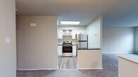 This single-floor unit offers a thoughtfully updated interior with a clean, neutral palette that creates a bright and welcoming atmosphere throughout. The standout feature is the renovated kitchen, which showcases crisp white shaker-style cabinetry accented with gold hardware, sleek dark granite countertops, and a eye-catching hexagonal tile backsplash. Stainless steel appliances — including a gas range, refrigerator, and dishwasher — are complemented by a wall-mounted range hood, while light wood-look flooring ties the space together. A skylight overhead fills the kitchen with natural light. The kitchen opens toward the living area via a partial wall with a built-in counter, creating a connected, functional layout. The living and bedroom spaces feature plush carpeting in neutral tones, offering comfort underfoot, and are bathed in natural light from multiple windows fitted with blinds. The bathroom is clean and functional, with a full-size soaking tub and shower combination, wood-look vinyl flooring, and a white vanity. Throughout the unit, neutral beige and white walls provide a versatile canvas, and the overall layout, as seen in the 3D dollhouse view, reflects a practical and efficient use of space.
