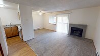 Located at 20283 1st Ave NE in Poulsbo, Washington, this single-floor unit offers a functional and comfortable layout with a clean, neutral aesthetic throughout. The open living area is carpeted and centers around a tile-surround fireplace, creating a warm focal point for the room. A ceiling fan overhead and a baseboard heating unit along the wall provide year-round comfort. Vertical blinds frame a sliding glass door that fills the space with natural light. The living area flows seamlessly into the kitchen, which features light wood cabinetry, laminate countertops, a double-basin sink, a dishwasher, and an electric range — all set on easy-care hardwood-style flooring. A dedicated hallway leads to the bedroom, which is carpeted and includes a window with blinds, a baseboard heater, and access to a full bathroom. The bedroom also benefits from proximity to in-unit laundry hookups, adding everyday convenience. Throughout the unit, textured ceilings and warm-toned wood door accents provide a consistent design language. The layout is efficient and well-organized, making excellent use of the available space while maintaining a bright, livable atmosphere suitable for a range of occupants.