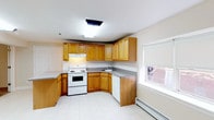 Located in Building 6 of Raritan Crossing, Unit #30 is a single-floor residence designed with a practical and open layout. The main living area is expansive and anchored by large light-toned floor tiles, with a structural column that subtly defines the space without closing it off. Baseboard heating units line the walls, and the entry door opens directly into this open-concept area, which flows seamlessly into the kitchen.

The kitchen is well-equipped with warm honey-toned oak cabinetry offering generous upper and lower storage, grey laminate countertops arranged in an L-shape, and white appliances including an electric range with overhead ventilation, a dishwasher, and a refrigerator. A window above the sink provides natural light, and the tile flooring continues throughout.

The bedroom features plush wall-to-wall carpeting, a ceiling fan with integrated lighting, and a pair of bifold closet doors offering ample storage. The room is bright and neutrally finished, lending itself well to various configurations.

The bathroom includes a full soaking tub with an overhead shower, clad in light beige ceramic tile surround, with a window for natural ventilation. Clean, neutral finishes throughout the unit create a cohesive and move-in ready environment.
