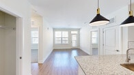 Located at 5270 Beechmont Ave in Cincinnati, Ohio, this single-floor unit offers a thoughtfully designed open-concept layout that seamlessly connects the kitchen and living areas. The kitchen is appointed with granite countertops, a subway tile backsplash, a stainless steel sink, and stylish black pendant lights with gold accents, creating a modern yet inviting atmosphere. Hardwood-style flooring flows throughout the main living spaces, complemented by crisp white walls and abundant natural light streaming through multiple windows. A door leads to a private balcony, further enhancing the bright and airy feel of the living area. The bedrooms are carpeted for added comfort and feature windows that bring in natural light. The primary bedroom connects to a dedicated bathroom and a walk-in closet equipped with wire shelving systems for organized storage. Additional bedrooms are well-proportioned with their own windows and plush carpeting. A dedicated laundry area includes a full-size washer and dryer alongside built-in shelving for extra storage. The overall design balances clean, contemporary finishes with functional living spaces throughout.