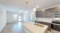 This single-floor, 2-bedroom, 2-bathroom residence in Gulf Breeze, Florida offers a clean, modern aesthetic throughout its thoughtfully designed layout. The open-concept living and kitchen area is anchored by light wood-look flooring, crisp white walls, and a ceiling fan that keeps the space comfortable and airy. Natural light flows in through large windows and a glass door leading to an outdoor area, enhancing the bright and welcoming ambiance.

The kitchen is a standout feature, equipped with dark espresso cabinetry, quartz countertops, a spacious center island with an undermount sink, elegant pendant lighting, and a full suite of stainless steel appliances including a refrigerator, electric range, and over-the-range microwave. Generous cabinet storage extends to the ceiling, maximizing functionality.

Both bedrooms are carpeted for comfort and include ceiling fans and windows that invite natural light. The primary bedroom connects to a well-appointed en-suite bathroom featuring a dual-sink vanity with quartz countertops, a glass-enclosed shower, wood-look flooring, and direct access to a walk-in closet with wire shelving. The second bathroom offers a single vanity and a shower-tub combination, maintaining the same clean, contemporary finishes found throughout the home.
