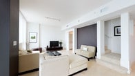 This two-story residence offers 2 bedrooms and 2.5 bathrooms thoughtfully arranged across a generous floor plan. The living area immediately impresses with its clean, modern aesthetic — featuring crisp white walls, smooth light-toned tile flooring, and an open layout that promotes an easy flow between spaces. A bold dark accent wall provides a striking focal point, adding depth and contrast to the otherwise bright, airy interior. Track lighting and recessed fixtures illuminate the space evenly, complementing the natural light throughout. The living room is well-proportioned, accommodating a full seating arrangement with room to spare, and connects seamlessly to adjacent areas. Architectural columns and thoughtful spatial zoning add character and structure to the open floor plan without compromising the sense of openness. The two and a half bathrooms provide practical convenience for residents and guests alike. Spanning two floors, the residence benefits from a clear separation between living and private spaces, enhancing both functionality and comfort. The overall ambiance is modern and understated, with a neutral palette and refined finishes that create a calm, sophisticated environment suitable for both everyday living and entertaining.