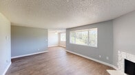 Located in Beaverton, Oregon, this two-bedroom, one-bathroom single-story home offers a well-organized and comfortable layout. The living room serves as the heart of the space, highlighted by a striking white stone fireplace and large windows that frame views of the surrounding greenery, filling the room with natural light. Wood-look flooring flows consistently throughout, complementing the cool gray tones of the walls and crisp white trim.

The galley-style kitchen is efficiently designed with white shaker cabinetry, dark speckled countertops, a double-basin sink, and white appliances including an electric range, refrigerator, and built-in microwave. A dedicated dining room sits adjacent, providing a defined space for meals. The entrance opens into a hallway that connects the main living areas to the private quarters.

Both bedrooms feature the same wood-look flooring and neutral gray walls, with windows providing natural light and views. The primary bedroom offers a generous footprint suitable for a full bedroom suite. Three closets throughout the home provide ample storage. The bathroom includes a white vanity with dark countertop and a large mirror. Textured ceilings are present throughout, and a ceiling fan in the living area adds to the home's functionality.