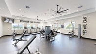 Located at 3640 Blue Fin Way in Fort Myers, Florida, this fitness center offers a generously sized, single-floor exercise space designed to support a full range of workout routines. The room features a clean, modern aesthetic with crisp white walls, recessed lighting, and tray ceiling details that lend a polished, well-maintained atmosphere throughout.

The facility is outfitted with an extensive selection of Matrix-brand strength equipment, including multi-station cable machines, a power rack with free weights, adjustable benches, a dumbbell rack, and a functional trainer. A dedicated cardio zone lines one wall with treadmills, ellipticals, and stair climbers, all positioned to take advantage of the abundant natural light streaming in through large windows and glass doors.

Large, modern ceiling fans are distributed throughout the space, ensuring comfortable air circulation during workouts. The durable rubber flooring provides both safety and functionality underfoot. Motivational phrases such as "Stronger Than Yesterday" and "As You Can" are displayed prominently on the walls, enhancing the energetic atmosphere.

Glass double doors open to an outdoor area with views of palm trees and the surrounding Florida landscape, connecting the interior to the natural environment. The combination of well-chosen equipment, thoughtful design, and ample natural light makes this fitness center a comprehensive and inviting workout destination.