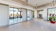 Located at 2021 Avenue Atwater in Montréal, this amenity floor offers a well-appointed recreational facility spanning a generous single level. At its centrepiece is a striking indoor swimming pool bathed in natural light from expansive floor-to-ceiling windows that frame panoramic views of the Montréal skyline. The pool area is elegantly finished with white ceramic tile surrounds, slatted ceiling detailing, ambient green accent lighting, and vibrant red potted plants that add a lively contrast to the crisp, bright interior. Colourful mosaic artwork adorns the walls, lending the space an artistic character. Poolside seating, including rattan lounge chairs, enhances the relaxed atmosphere.

The fitness centre is a well-equipped, modern exercise room featuring rubber flooring, full-wall mirrors, and a comprehensive selection of equipment including cable machines, treadmills, ellipticals, stationary bikes, and a full dumbbell rack. Large skylights and oversized windows flood the space with natural light and offer city views, creating an energizing workout environment. A bold athletic mural adds visual dynamism to the room.

Connecting these amenities is a welcoming hallway finished with distinctive hexagonal mosaic tile flooring, globe pendant lighting, and views onto an exterior spiral staircase, completing this thoughtfully designed recreational facility.