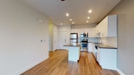This well-appointed single-floor residence offers a thoughtfully designed open-concept layout that seamlessly connects the kitchen and living areas. The kitchen is a standout feature, showcasing crisp white cabinetry, light gray subway tile backsplash, and a full suite of stainless steel appliances including a refrigerator, range with oven, and built-in microwave. A central island with a dark quartz-style countertop provides additional workspace and casual dining potential. Warm hardwood-style flooring runs throughout the main living and kitchen areas, adding a welcoming contrast to the bright, neutral walls and recessed lighting overhead.

The bedroom is generously sized, finished with soft neutral carpeting and painted in a calming gray tone. A ceiling fan with integrated lighting adds both comfort and function, while a window frames views of the surrounding cityscape, filling the room with natural light.

The bathroom is clean and functional, featuring white cabinetry with a dark countertop, a large mirror, and a full soaking tub with shower surround. Tile-style flooring completes the space with a practical, contemporary finish. Overall, the unit presents a modern, move-in-ready aesthetic with consistent finishes throughout.