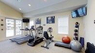 This single-floor fitness room offers a practical and well-organized space for exercise, outfitted with a variety of cardio and strength equipment. The room features treadmills, an elliptical trainer, and a recumbent stationary bike, providing options for users of varying fitness levels and preferences. Exercise balls and a step platform are also available, supporting flexibility, balance, and low-impact training routines.

The walls are painted in a warm neutral tone, contributing to an inviting atmosphere. Motivational fitness artwork is displayed prominently, adding an energetic visual element to the space. Two wall-mounted flat-screen televisions are positioned for easy viewing during workouts, enhancing the overall exercise experience.

Natural light enters through multiple windows fitted with white horizontal blinds, keeping the space bright while allowing for privacy and glare control. Recessed ceiling lighting supplements the natural light, ensuring the room remains well-lit at all times. The flooring is a durable, textured carpet suited for fitness use. Overall, the space is thoughtfully arranged to maximize functionality while maintaining a clean and welcoming environment.