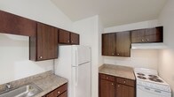 This single-story space presents a clean, open layout with a bright and airy ambiance throughout. Light-toned ceramic tile flooring flows consistently across the living areas, complementing the crisp white walls and creating a cohesive, well-lit interior feel.

The main living area stands out with notably vaulted ceilings that amplify the sense of space and openness. Recessed lighting and a ceiling fan provide both illumination and comfort, while a hallway leads toward a window at the far end, drawing in natural light and offering views of the outdoors. A secondary room features its own window overlooking a lush outdoor setting with tropical vegetation, further enhancing the natural brightness of the space.

The kitchen is efficiently designed with rich, dark-stained wood cabinetry spanning both upper and lower sections, offering generous storage. Granite-style countertops provide durable work surfaces, while white appliances including a refrigerator and electric range complete the functional setup. Light tile flooring continues into this area, maintaining visual consistency.

The bathroom is neatly appointed with a granite-topped vanity, a large mirror, tile flooring, and a combination shower and bathtub, providing a clean and practical design. Overall, the space offers a straightforward, functional layout with warm and welcoming details throughout.