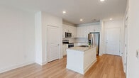 Located at 3025 Woodward Crossing Blvd in Buford, GA, this well-designed one-bedroom residence offers a thoughtfully arranged single-floor layout. The open-concept kitchen and living area serves as the heart of the home, finished with light wood-style flooring that runs throughout the main spaces. The kitchen is equipped with stainless steel appliances, including a refrigerator with ice maker, electric range, and over-the-range microwave. Crisp white shaker cabinetry extends to the ceiling, providing generous storage, while granite countertops and a central island with an integrated sink add both functionality and style. Recessed lighting illuminates the space throughout. The living area extends toward a sliding glass door that fills the room with natural light and offers outdoor views. The spacious primary bedroom features soft carpet flooring, a ceiling fan, and a window with outdoor views, creating a comfortable and well-lit retreat. A dedicated laundry room houses a full-size washer and dryer with overhead shelving for additional storage. Clean white walls, modern finishes, and a bright, neutral palette give the entire residence a fresh and contemporary feel.