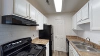 This single-floor, 2-bedroom, 1.5-bathroom residence offers a functional and practical layout designed for comfortable everyday living. The galley-style kitchen is well-equipped, featuring white cabinetry with brushed nickel hardware, granite-style laminate countertops, a white subway tile backsplash, and a full suite of black appliances including an electric range, refrigerator, and dishwasher. Wood-look flooring runs throughout the kitchen, adding warmth and durability to the space.

The living room is generously sized, featuring plush carpeting and a wide sliding glass door flanked by vertical blinds, allowing an abundance of natural light and providing views of the outdoor greenery beyond. This space feels open and airy, well-suited for both relaxing and entertaining.

Both bedrooms are carpeted and offer ample wall space, with each room receiving natural light through windows. One bedroom features a ceiling fan with light fixture, while the other includes a closet and window with outdoor views.

The full bathroom includes a tiled tub and shower combination, while the half bathroom provides a toilet and vanity in a compact, neutral-toned space. Throughout the unit, neutral wall tones and consistent finishes create a cohesive and move-in-ready atmosphere.