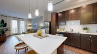 This single-story, one-bedroom residence offers a thoughtfully designed open-concept layout that maximizes its efficient footprint. The combined kitchen and living area forms the heart of the unit, anchored by a prominent central island with a quartz countertop and seating — ideal for casual dining or entertaining. The kitchen is outfitted with rich dark-espresso cabinetry extending to the ceiling, a classic white subway tile backsplash, stainless steel appliances including a refrigerator, range, microwave, and dishwasher, all complemented by wood-style flooring. Track lighting and pendant lights over the island provide layered illumination throughout the space. The living area flows naturally from the kitchen, offering a bright, open feel enhanced by natural light from large windows. The bedroom features soft carpeting, a ceiling fan, large windows that invite ample daylight, and neutral gray accent walls. A dedicated walk-in closet serves the bedroom, featuring built-in shelving and dual hanging rods for organized storage. A hallway connects the main living areas to the private bedroom, providing a clear and functional circulation path throughout the residence.