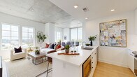 This contemporary single-floor residence blends industrial and modern design elements to create a refined, light-filled living environment. Exposed concrete ceilings throughout lend an urban loft character, contrasting beautifully with crisp white walls and warm light wood flooring.

The open-concept living, dining, and kitchen area forms the heart of the space. The kitchen is outfitted with sleek white cabinetry extending to the ceiling, quartz countertops, stainless steel appliances, a built-in cooktop, and a generously sized island with seating — ideal for both everyday living and entertaining. The living and dining areas are bathed in natural light from large windows on multiple sides, offering sweeping city and treetop views.

Two well-appointed bedrooms each feature the signature exposed concrete ceilings, large windows with city views, light wood flooring, and a serene, neutral palette. Both rooms are connected to thoughtfully designed bathrooms showcasing striking geometric patterned tile floors, white vanities with brass fixtures, globe sconce lighting, and full-length mirrors. The primary bathroom includes a glass-enclosed walk-in shower with full subway tile surround.

A clean hallway connects the private and common areas, maintaining a logical and comfortable flow throughout this sophisticated urban residence.