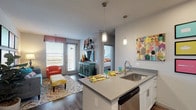 This single-story residence offers a well-organized, open-concept layout that connects the kitchen, dining, and living areas into one cohesive space. The kitchen is outfitted with white shaker-style cabinetry, quartz-style countertops, a stainless steel appliance suite including a refrigerator, electric range, built-in microwave, and dishwasher, as well as a tiled backsplash. A peninsula with an undermount sink provides additional workspace and serves as a natural divider between the kitchen and the living area. Pendant lighting above the peninsula adds a contemporary touch. Wood-style plank flooring extends throughout the main living areas, lending warmth and visual continuity.

The living room receives natural light through a large window overlooking an exterior balcony, creating a bright and inviting atmosphere. The bedroom is a comfortable retreat featuring plush carpeting, a ceiling fan, and a generous window dressed with decorative curtains. The bathroom is finished with wood-style flooring, a single vanity with white cabinetry, and a glass-enclosed walk-in shower with tile surround. The unit also features a private entry door and neutral gray walls throughout, providing a versatile backdrop.