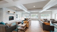 This well-appointed single-story clubhouse is designed to serve as a versatile community hub, blending social and functional spaces within a cohesive, contemporary interior. The main lounge area is an expansive, light-filled room anchored by a striking white stone fireplace and characterized by elegant coffered ceilings with recessed lighting. Large windows along the rear wall offer direct views of an outdoor pool area, filling the space with natural light. The flooring transitions between warm wood-look planks and large-format tile, helping to define different zones throughout the facility.

The lounge accommodates multiple seating arrangements, including leather sofas, teal accent chairs, and a dining area with a wall-mounted television — ideal for casual gatherings. A dedicated media lounge features additional mounted TVs and curated wall art. The business center provides a professional setting with round conference tables, ergonomic seating, a wall-mounted display screen, and carpeted flooring for acoustic comfort.

The kitchen is fully equipped with white shaker cabinetry, dark granite countertops, stainless steel appliances including a refrigerator and dishwasher, and a coffee station. The entry foyer features large-format tile flooring and glass doors with pool-area views, creating a welcoming first impression throughout.