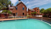 This community amenity space offers residents a comprehensive fitness and recreation experience. The outdoor pool area is a standout feature, showcasing a generously sized swimming pool with clear turquoise water, enclosed by a black iron fence and surrounded by a brick paver deck lined with lounge chairs. The backdrop of classic multi-story brick buildings adds a timeless architectural character to the outdoor setting.

The fitness center is thoughtfully designed to support a wide variety of workout styles. The space is bright and airy, benefiting from abundant natural light streaming through multiple large windows that offer views of the surrounding community. Elevated ceilings and full-length mirrored walls enhance the sense of openness throughout.

The gym is outfitted with a comprehensive selection of equipment, including Precor cardio machines, treadmills, a rowing machine, a multi-functional cable and strength system, a squat rack with bench, a full dumbbell rack, medicine balls, battle ropes, and stability balls. Ceiling fans provide added comfort during workouts. The patterned herringbone carpet flooring adds a modern, polished aesthetic to the interior. Together, the pool and fitness center form a well-rounded amenity suite designed to support an active lifestyle.