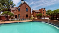 This community amenity space offers residents a comprehensive fitness and recreation experience. The outdoor pool area is a standout feature, showcasing a generously sized swimming pool with clear turquoise water, enclosed by a black iron fence and surrounded by a brick paver deck lined with lounge chairs. The backdrop of classic multi-story brick buildings adds a timeless architectural character to the outdoor setting.

The fitness center is thoughtfully designed to support a wide variety of workout styles. The space is bright and airy, benefiting from abundant natural light streaming through multiple large windows that offer views of the surrounding community. Elevated ceilings and full-length mirrored walls enhance the sense of openness throughout.

The gym is outfitted with a comprehensive selection of equipment, including Precor cardio machines, treadmills, a rowing machine, a multi-functional cable and strength system, a squat rack with bench, a full dumbbell rack, medicine balls, battle ropes, and stability balls. Ceiling fans provide added comfort during workouts. The patterned herringbone carpet flooring adds a modern, polished aesthetic to the interior. Together, the pool and fitness center form a well-rounded amenity suite designed to support an active lifestyle.