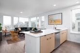 This contemporary urban residence is thoughtfully designed across a single floor, offering a seamless blend of modern finishes and inviting style. The open-concept living and kitchen area serves as the heart of the home, where a large wraparound window wall floods the space with natural light and frames impressive city and skyline views. The kitchen features light wood cabinetry, crisp white quartz countertops, stainless steel appliances, a subway tile backsplash, and a central island that doubles as a breakfast bar — ideal for both casual dining and entertaining. Wide-plank wood-tone flooring runs throughout, unifying the space with warmth and continuity. The living area is generously proportioned, anchored by a corner window arrangement that maximizes the urban panorama. The primary bedroom is a serene retreat, highlighted by a striking art deco-inspired wallpapered accent wall, a large window with neighborhood views, and direct access to the hallway. The full bathroom is finished with a floating wood vanity, a large format mirror, white quartz countertop, and a full tub and shower combination. Completing the layout is a dedicated in-unit laundry closet with a stacked washer and dryer, adding a practical and convenient touch to this well-appointed urban home.