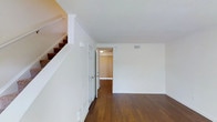 This two-story residence offers a well-organized layout across two levels, designed to maximize functionality and comfort. The main living area is finished with rich hardwood flooring that extends throughout, providing warmth and visual continuity against the crisp white walls. Crown molding adds a refined architectural detail along the ceiling lines, contributing a classic touch to the otherwise clean, neutral aesthetic.

A staircase with carpet-covered treads connects the two floors, conveniently accessible from the main living space. The open corridor leading toward additional rooms is bright and welcoming, with natural light filtering in through window treatments visible in the adjoining space. HVAC vents are thoughtfully integrated into the ceiling, ensuring climate comfort throughout.

The overall ambiance of the space is light, airy, and move-in ready, with a straightforward layout that allows for flexible furniture arrangements. The two-bedroom, two-bathroom configuration provides practical accommodations, with the two-level design offering a natural separation between living and private spaces. The neutral palette throughout serves as a versatile canvas for a variety of interior styles.