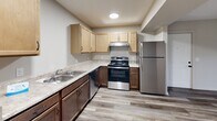 Located at 1800 Commerce Pkwy in La Grange, Kentucky, this single-level, one-bedroom, one-bathroom unit offers a thoughtfully organized layout designed for comfortable everyday living. The open-concept main area seamlessly combines the living room, dining space, and kitchen into one cohesive zone. The living area features rich dark wood-look flooring and a sliding glass door that fills the space with natural light while offering outdoor views. The kitchen is well-appointed with two-toned cabinetry — light upper cabinets and rich dark lower cabinets — complemented by stainless steel appliances including a range, dishwasher, and refrigerator, along with ample counter space and a double sink. The bedroom is carpeted for warmth and comfort, with a window that brings in additional natural light. The bathroom includes a dark wood vanity with a large mirror and wood-look flooring. A dedicated laundry room with washer and dryer hookups adds everyday convenience. Two closets provide generous storage throughout the unit, and a utility room rounds out the functional floor plan. Neutral tones and clean finishes throughout give the space a fresh, move-in-ready feel.