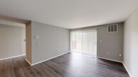 This single-floor unit offers a thoughtfully designed layout encompassing a combined kitchen and living room, one bedroom, one bathroom, a dedicated closet, and a hallway connecting the spaces. The living room is a bright, open area finished with dark hardwood-style flooring and neutral gray walls. A large sliding glass door fitted with vertical blinds serves as the room's focal point, allowing generous natural light and providing outdoor access. A ceiling fan is visible from the hallway entry, adding both function and subtle character.

The kitchen is efficiently arranged in an L-shaped configuration, featuring dark cabinetry, light countertops, a subway tile backsplash, and stainless steel appliances including a gas range, dishwasher, and over-range microwave. A window above the sink brings in additional natural light. The kitchen transitions seamlessly into the living area via light-toned hardwood-style flooring.

The bedroom is a well-sized, carpeted room finished in the same neutral gray palette. It includes access to a dedicated walk-in closet with built-in shelving and a direct connection to the hallway. The bathroom features a full tub-shower combination with striking vertically-laid gray tile surround, wood-look tile flooring, a white vanity, and brushed nickel fixtures, delivering a clean, contemporary aesthetic throughout.