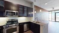 Located on Westheimer Road in Houston's vibrant Galleria area, this one-bedroom, one-bathroom residence blends contemporary design with industrial-chic character. The living area makes a bold statement with a full exposed brick accent wall and expansive floor-to-ceiling windows that flood the space with natural light and frame open city views, including the Houston skyline. Rich wood-look flooring runs throughout, complementing the warm and modern aesthetic.

The kitchen is well-appointed with dark espresso cabinetry featuring frosted glass upper panels, granite countertops, a classic subway tile backsplash, and a full suite of stainless steel appliances including a gas range, built-in microwave, dishwasher, and a side-by-side refrigerator with an in-door ice and water dispenser. A mosaic tile accent wall adds a striking visual element, while pendant lighting over the sink enhances the functional elegance.

The bedroom is a bright, tranquil retreat with large windows offering outdoor views and ample natural light. A dedicated closet provides practical storage. The bathroom is finished with neutral tile, a granite-topped vanity with dark cabinetry, and a full soaking tub. A hallway connects the rooms, contributing to a well-organized and efficient layout ideal for urban living.