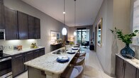Located in the sought-after Montrose/River Oaks corridor of Houston, this single-floor residence at 1916 W Gray St offers a thoughtfully designed layout with contemporary finishes throughout. The kitchen is a standout feature, showcasing rich dark-stained cabinetry extending to the ceiling, light granite countertops, a subway tile backsplash with under-cabinet lighting, and a full suite of stainless steel appliances including a French door refrigerator, range, and built-in microwave. A diamond-pattern wine rack adds a refined touch overhead. The kitchen flows seamlessly into a dining area anchored by a granite waterfall island with bar seating and elegant pendant lighting, creating an ideal space for entertaining. The living room is bathed in natural light from floor-to-ceiling windows and a glass sliding door that opens to a private balcony with outdoor views. The bedroom features large black-framed windows overlooking a landscaped courtyard, providing a serene retreat. The bathroom is finished with dark granite vanity countertops, a soaking tub, a separate glass-enclosed shower, and classic tile flooring. Neutral gray tones and large-format tile floors unite the space in a cohesive, modern aesthetic throughout.