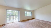 This single-floor residence offers a well-organized layout with a clean, neutral aesthetic throughout. The spacious living area is a standout feature, highlighted by vaulted ceilings, plush wall-to-wall carpeting, and an abundance of natural light streaming in through large windows and a sliding glass door that opens to a private balcony overlooking mature, verdant landscaping. The open sightlines between the living area and dining space create a comfortable, connected flow, with the dining area accented by a classic chandelier. The galley-style kitchen is efficiently designed with white cabinetry, ample counter space, light wood-look flooring, a double sink, and white appliances including a refrigerator and electric range. A dedicated in-unit laundry area provides added convenience with full-size washer and dryer connections and overhead shelving. The bedrooms feature plush carpeting and sliding-door closets with built-in hanging rods. Two bathrooms serve the unit: a full bathroom with a single vanity, large mirror, and soaking tub, and a second bathroom equipped with a walk-in shower featuring sliding glass doors. Light wood-look flooring carries through the kitchen, bathrooms, and laundry area, providing a cohesive and easy-to-maintain finish throughout the non-carpeted spaces.