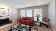 This single-story residence offers a thoughtfully designed layout with comfortable living spaces throughout. The living room serves as a central gathering area, featuring a tile-surround fireplace, plush carpeting, and a bank of three windows fitted with horizontal blinds that draw in natural light. A large closet with bifold doors provides additional storage within this space.

The dining area connects seamlessly to the kitchen via a pass-through counter, creating an open feel between the two spaces. A ceiling fan with light fixture illuminates the dining room, which accommodates a round table and is complemented by a window and access to the exterior. The kitchen is equipped with warm oak cabinetry, light speckled countertops, and black appliances including an electric range with overhead ventilation.

The bedrooms are carpeted and include ceiling fans with lighting, windows for natural light, and ample room for furnishings. The primary bathroom features an extended wood-toned vanity topped with a speckled countertop, a large wall mirror with overhead globe lighting, and hardwood-style flooring, creating a functional and polished space. Neutral wall tones and textured ceilings are consistent throughout, lending cohesion to the overall design.