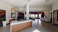 This vibrant community clubhouse at Ely offers a thoughtfully designed amenity space that blends bold aesthetics with practical functionality. The welcoming lobby greets visitors with a striking marble-topped reception desk featuring a warm wood and gold accent base, complemented by sculptural geometric pendant lighting and rich burgundy accent walls. A life-size black horse sculpture and curated artwork add a distinctive, artistic character throughout the space.

The game room is a standout feature, boasting dramatic circular tiered ceiling details in dark charcoal, a full-size billiards table, foosball tables, arcade games, and a vinyl record-themed feature wall that creates an energetic, entertainment-focused atmosphere. An adjacent lounge and kitchenette area provides a casual gathering space with bar-height seating, pendant lighting, and subway tile backsplash details.

The fitness center is comprehensively equipped with cardio machines including treadmills and stationary bikes, a full dumbbell rack, and multiple cable and strength training machines. Wall-mounted TVs, large windows offering natural light, and a water station complete the workout experience.

Outdoors, a generously sized resort-style swimming pool is surrounded by lounge chairs, egg-shaped hanging seats, string lights, and privacy curtains, creating a relaxed and social outdoor retreat.