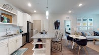 This single-floor residence offers a thoughtfully designed open-concept layout that seamlessly connects the kitchen, dining, and living areas. The kitchen is a standout feature, showcasing white shaker cabinetry, granite countertops, a subway tile backsplash, and a full suite of stainless steel appliances. A central island with built-in shelving provides additional storage and bar seating, making it an ideal space for both cooking and casual dining. Wood-look flooring flows throughout the main living areas, adding warmth and continuity to the space.

The living room is bright and welcoming, featuring large windows that invite natural light and a ceiling fan overhead. Two well-proportioned bedrooms offer plush carpeting and ample room for comfortable furnishings. Each bathroom is finished to a high standard, featuring granite-topped white vanities, wood-look flooring, and full tub-shower combinations with clean tile surrounds. The primary bathroom includes a double vanity and additional space for a separate shower.

The overall aesthetic is modern and cohesive, with neutral tones, recessed lighting, and clean architectural lines throughout. The combination of functional design and quality finishes makes this a comfortable and visually appealing residence.