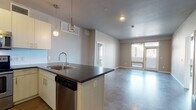 Located at 3490 Larimer St in Denver's RiNo neighborhood, this single-floor unit presents a contemporary urban design defined by polished concrete floors throughout and a neutral, modern color palette. The open-concept layout connects the kitchen and living area seamlessly, creating a spacious, flexible environment well-suited for both everyday living and entertaining.

The kitchen features a peninsula with a dark countertop and an undermount double sink, pendant lighting overhead, and a full suite of stainless steel appliances, including a refrigerator, range, microwave, and dishwasher. Light wood cabinetry with brushed metal hardware and a tile backsplash complete the contemporary aesthetic.

The living area is generously proportioned, benefiting from large sliding glass doors and floor-to-ceiling windows that invite abundant natural light and provide views of the surrounding Denver cityscape. The open floor plan transitions smoothly into the private bedroom areas, each featuring large windows with urban views and ceiling fans.

The bathrooms are finished with dark countertops, light wood vanity cabinetry, vessel-style sinks, large mirrors, and walk-in showers with glass enclosures, maintaining the consistent modern design language found throughout the space.
