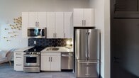 Located at 1402 Winnifred St in Charlotte, NC's vibrant Dilworth neighborhood, this contemporary studio is thoughtfully designed to maximize both function and style. The open-concept layout seamlessly connects the living, sleeping, and dining areas, creating a versatile and efficient use of space. Large windows flood the room with natural light and offer pleasant outdoor views, enhancing the bright and airy ambiance.

The galley-style kitchen is a standout feature, outfitted with stainless steel appliances including a French door refrigerator, gas range, built-in microwave, and dishwasher. White shaker cabinetry extends to the ceiling for ample storage, while granite countertops and a bold black hexagonal tile backsplash add a modern, polished aesthetic. Dark hardwood-style flooring runs throughout, providing a cohesive and contemporary foundation.

The bathroom echoes the same modern design language, featuring a granite-topped vanity with white cabinetry, matte black hardware, a framed mirror, and a pendant light fixture for a refined touch. The living and sleeping area is defined by curated wall art, warm lighting, and a compact dining nook, demonstrating smart use of the available space. Recessed lighting throughout ensures a well-lit environment at all times.