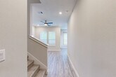 Located in Katy, Texas, this two-story home offers a thoughtfully designed layout spread across two floors. The main level features an open-concept living area and kitchen, finished with light-toned wood-look flooring throughout. The kitchen is a standout, boasting rich dark-stained cabinetry, granite countertops, a center island with a sink, stainless steel appliances including a French door refrigerator and gas range, and open floating shelves — all bathed in natural light from large windows with white blinds. The living area flows seamlessly from the kitchen, with recessed lighting and a staircase connecting to the upper floor. Upstairs, the primary bedroom is generously sized and includes a ceiling fan, wood-look flooring, and ample natural light. The en-suite primary bathroom features a dual-sink vanity with dark cabinetry, white countertops, tile flooring, and a separate water closet. Two additional bedrooms are finished with plush carpeting and feature windows that bring in natural light, with one bedroom offering a double-door closet. A full bathroom serves the secondary bedrooms. Throughout the home, neutral tones, clean lines, and modern hardware create a cohesive and inviting atmosphere.