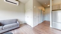 This thoughtfully designed 460-square-foot studio apartment at 126 Langdon Street in Madison, Wisconsin offers an efficient single-floor layout incorporating a kitchen, living area, and dedicated laundry space. Light hardwood-style flooring runs throughout, creating a cohesive and airy feel across the entire unit.

The kitchen is a standout feature, outfitted with taupe cabinetry, white subway tile backsplash, stainless steel appliances including a range and dishwasher, and a full-size refrigerator. Open shelving adds a modern touch, while a geometric peninsula with a white countertop provides additional prep space and bar-height seating for two beneath a striking white-and-gold dome pendant light.

The living area benefits from large, floor-to-ceiling windows that flood the space with natural light and frame views of the Madison skyline, including a glimpse of the State Capitol. A wall-mounted ductless HVAC unit ensures year-round climate comfort. Multiple closets along an interior hallway offer ample storage for a compact unit.

The in-unit laundry area houses a stacked Whirlpool washer and dryer alongside wire shelving for added convenience. Clean lines, neutral tones, and modern fixtures throughout give this studio a polished, contemporary character well-suited to urban living.