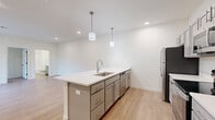 This single-story, one-bedroom, one-bathroom residence offers a thoughtfully designed open floor plan that maximizes its comfortable footprint. The interior is finished with light wood-style luxury vinyl plank flooring in the main living areas, contributing to a bright, clean aesthetic throughout.

The combined kitchen and living room serves as the heart of the home. The kitchen is outfitted with stainless steel appliances, including a refrigerator, electric range, and over-the-range microwave, complemented by gray shaker-style cabinetry and white quartz countertops. A central island with a built-in sink and pendant lighting overhead provides both additional workspace and a casual dining option, while a sliding glass door in the living area invites natural light and provides outdoor access.

The bedroom features neutral carpet flooring and includes a double-door closet for storage. Recessed lighting and a connected full bathroom with additional closet access enhance the room's functionality.

The bathroom is finished with light wood-style flooring, a gray vanity with white countertop, and a full shower-tub combination. A dedicated laundry room houses a full-size washer and dryer with overhead wire shelving, adding significant everyday convenience to the unit.