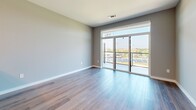 Located at 1 West Ave in Kannapolis, NC, this thoughtfully designed one-bedroom, one-bathroom residence offers a modern aesthetic throughout its efficiently utilized single-floor layout. The open-concept living and kitchen area serves as the heart of the home, where wide-plank hardwood-style flooring flows seamlessly underfoot. The kitchen is outfitted with dark wood cabinetry, stainless steel appliances, a white quartz countertop island with an undermount sink, and a matte black faucet, all illuminated by stylish glass pendant lights. A wood-accented ceiling detail adds warmth and visual interest to the space. The living area extends toward a full-width sliding glass door that opens to a private balcony with a railed surround, allowing abundant natural light and open outdoor views to fill the room. The bedroom features soft carpeting, a ceiling fan, and a generous window overlooking the surrounding landscape. The bathroom presents a clean, contemporary design with large-format tile flooring, a wood-toned vanity with white countertop, an illuminated mirror, and matte black hardware accents throughout. Soft gray wall tones unify the entire residence, creating a calm and cohesive living environment.