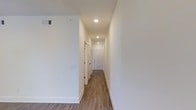 This single-floor residence offers a thoughtfully arranged 1-bedroom, 1-bathroom layout that maximizes functionality and comfort. The interior is finished with clean, contemporary details that create a bright and welcoming atmosphere throughout.

A central hallway serves as the spine of the home, connecting the various rooms with ease. The corridor features recessed lighting set into smooth white ceilings, casting an even, warm glow across the space. Crisp white walls and clean white baseboards run the length of the hallway, complementing the warm-toned wood-look flooring that extends seamlessly underfoot. The flooring adds a grounded, natural warmth to the otherwise light and airy interior palette.

White panel doors line the hallway, providing access to the bedroom, bathroom, and additional spaces within the unit. The overall design is minimal and modern, with a neutral color scheme that offers a versatile backdrop for a variety of furnishing styles.

The layout makes efficient use of its footprint, ensuring that each area feels purposeful and well-proportioned. Natural light and recessed ceiling fixtures combine to keep the interior feeling open and pleasant. This residence presents a clean, move-in-ready space with consistent finishes and a practical, livable design.