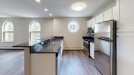 This single-floor unit is defined by a cohesive neutral palette and a mix of practical and architectural details that create a comfortable, well-organized living space. The open-concept living and kitchen area serves as the heart of the unit, where hardwood-style flooring flows seamlessly underfoot. The kitchen is equipped with stainless steel appliances, including a gas range, microwave, and refrigerator, complemented by white cabinetry and dark granite-style countertops. A peninsula with bar seating separates the kitchen from the living area, enhancing the open feel. A distinctive circular accent window above the range and arched windows throughout the unit admit generous natural light and add architectural character to the otherwise straightforward design. Recessed lighting and flush-mount ceiling fixtures provide reliable illumination throughout.

The living area benefits from multiple arched windows framing exterior views, while a ceiling fan adds comfort. Bedrooms feature plush carpeting, neutral wall tones, and sliding mirrored closet doors that reflect light and enhance the sense of space. The bathroom includes a full tub-and-shower surround in a clean white finish with a built-in shelf and chrome fixtures. Baseboard heating is present throughout, ensuring consistent warmth.